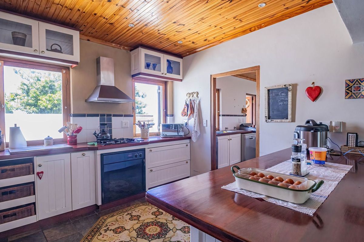 A rustic-style kitchen featuring timber ceilings, white cabinetry, timber countertops, and a built-in oven with gas hob, offering a warm and functional cooking space.