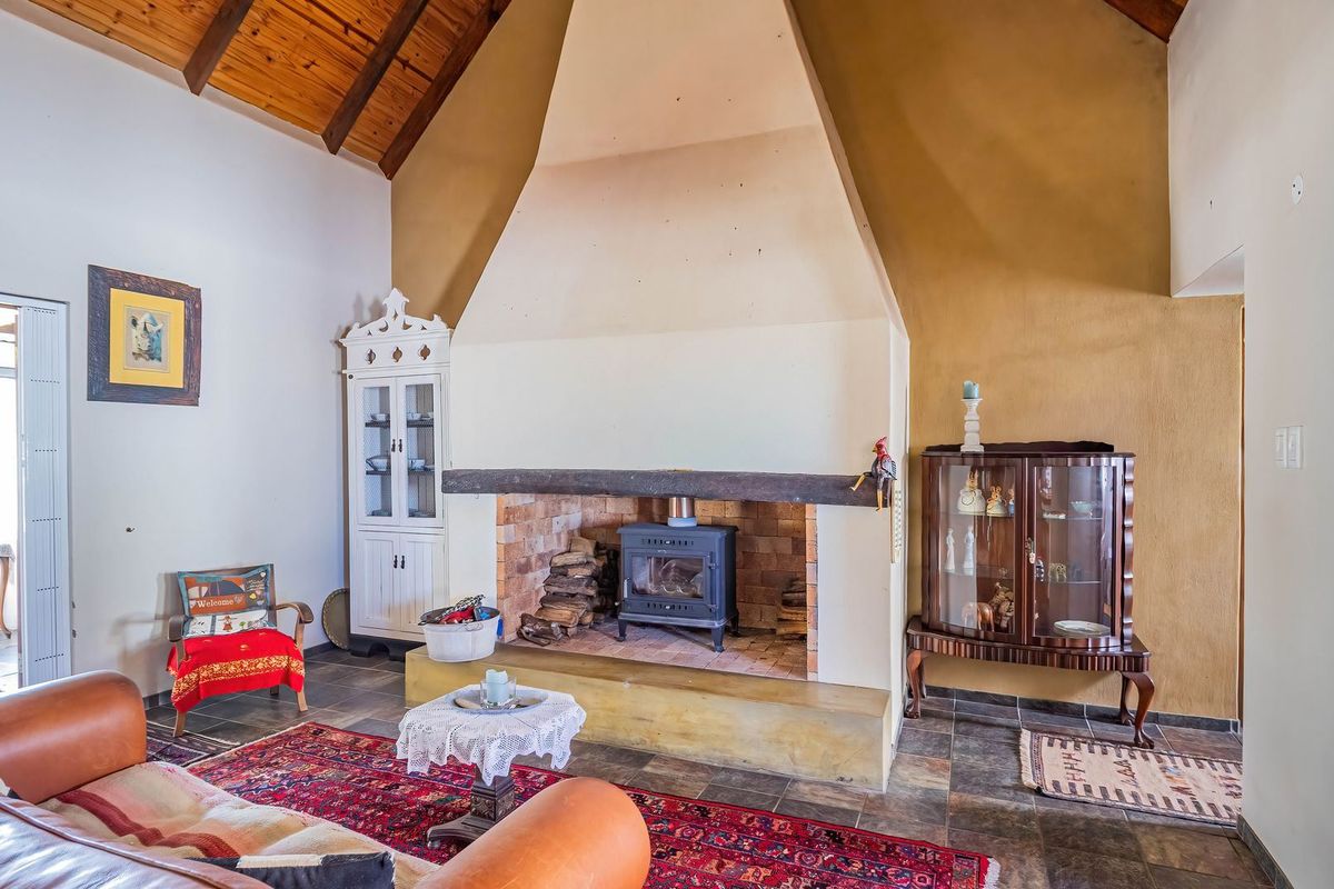 Spacious living room featuring a prominent masonry fireplace with a wood-burning stove, vaulted timber ceilings, and durable stone tile flooring.