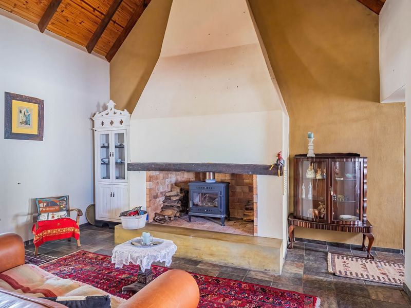 Spacious living room featuring a prominent masonry fireplace with a wood-burning stove, vaulted timber ceilings, and durable stone tile flooring.