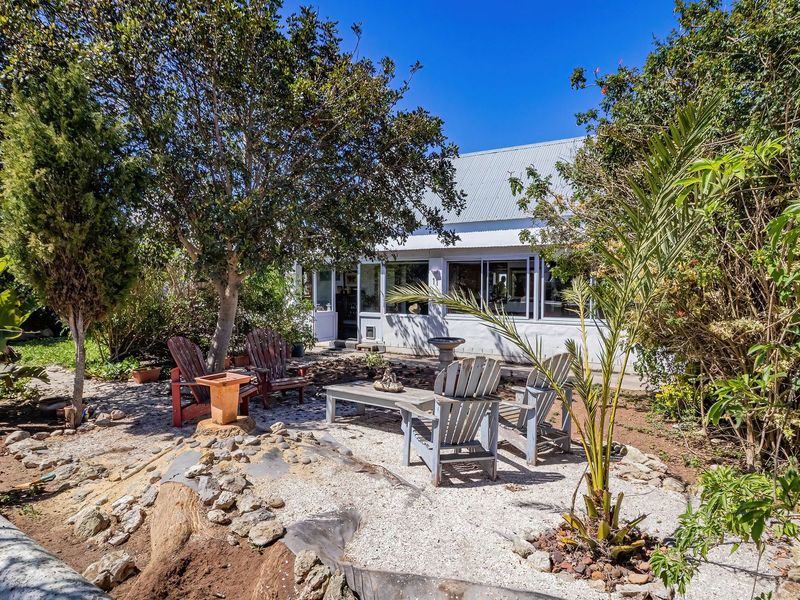 A private rear garden area featuring gravel landscaping, mature trees, and a view of the home's rear facade with large windows and a metal roof.