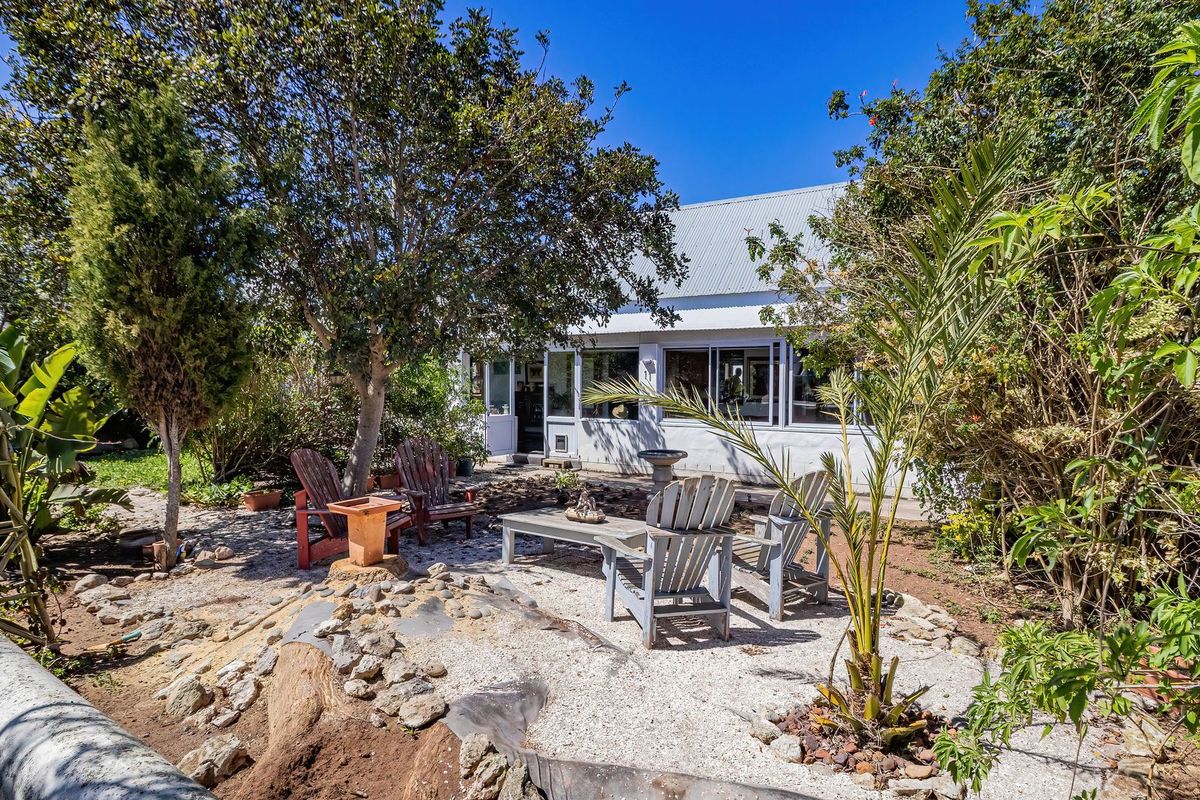 A private rear garden area featuring gravel landscaping, mature trees, and a view of the home's rear facade with large windows and a metal roof.