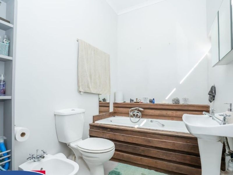 A functional bathroom featuring a built-in bathtub with wood-panelled surround, pedestal basin, toilet, bidet, and integrated shelving units.