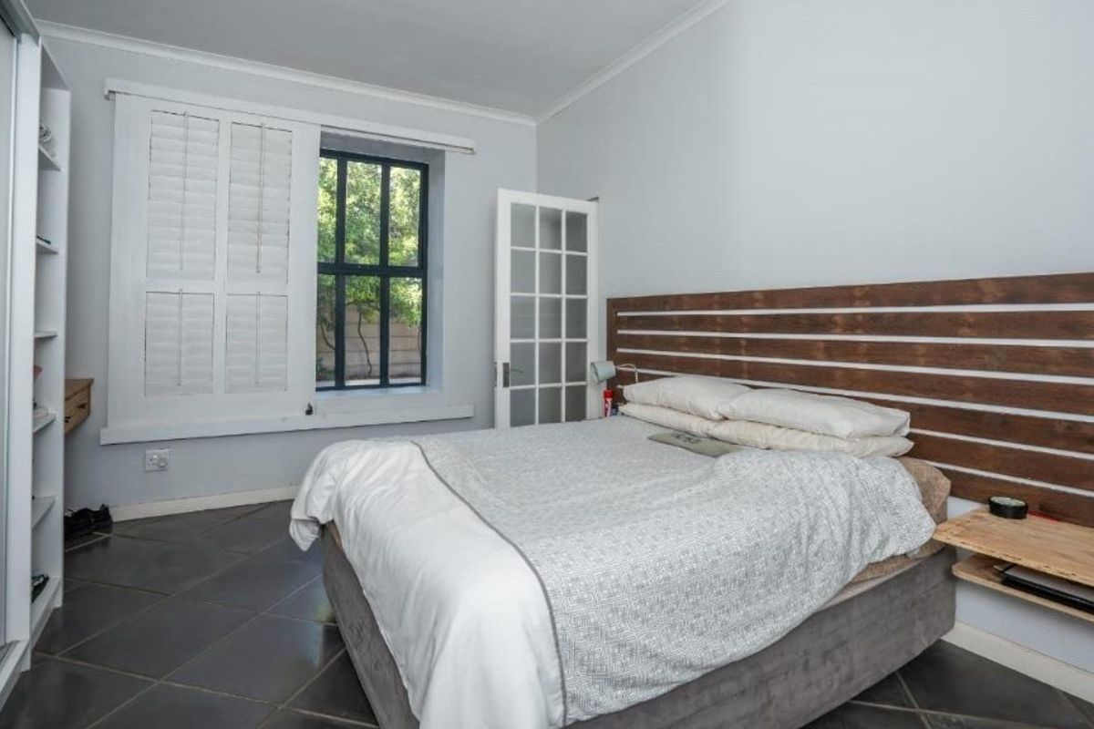 A well-lit bedroom featuring tiled flooring, plantation shutters, and a built-in wardrobe, offering a clean and functional living space.