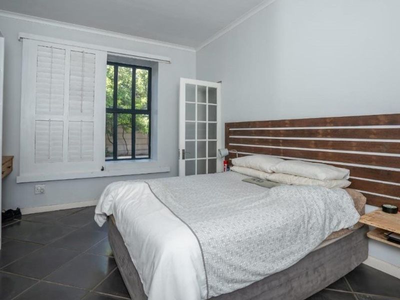 A well-lit bedroom featuring tiled flooring, plantation shutters, and a built-in wardrobe, offering a clean and functional living space.