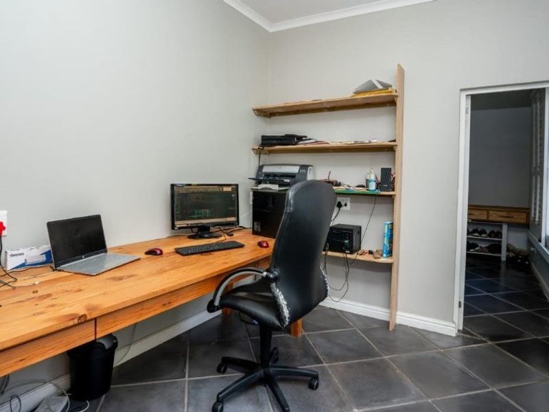 A functional home office space featuring a built-in wooden desk, wall-mounted shelving, and durable tiled flooring, providing a practical workspace.