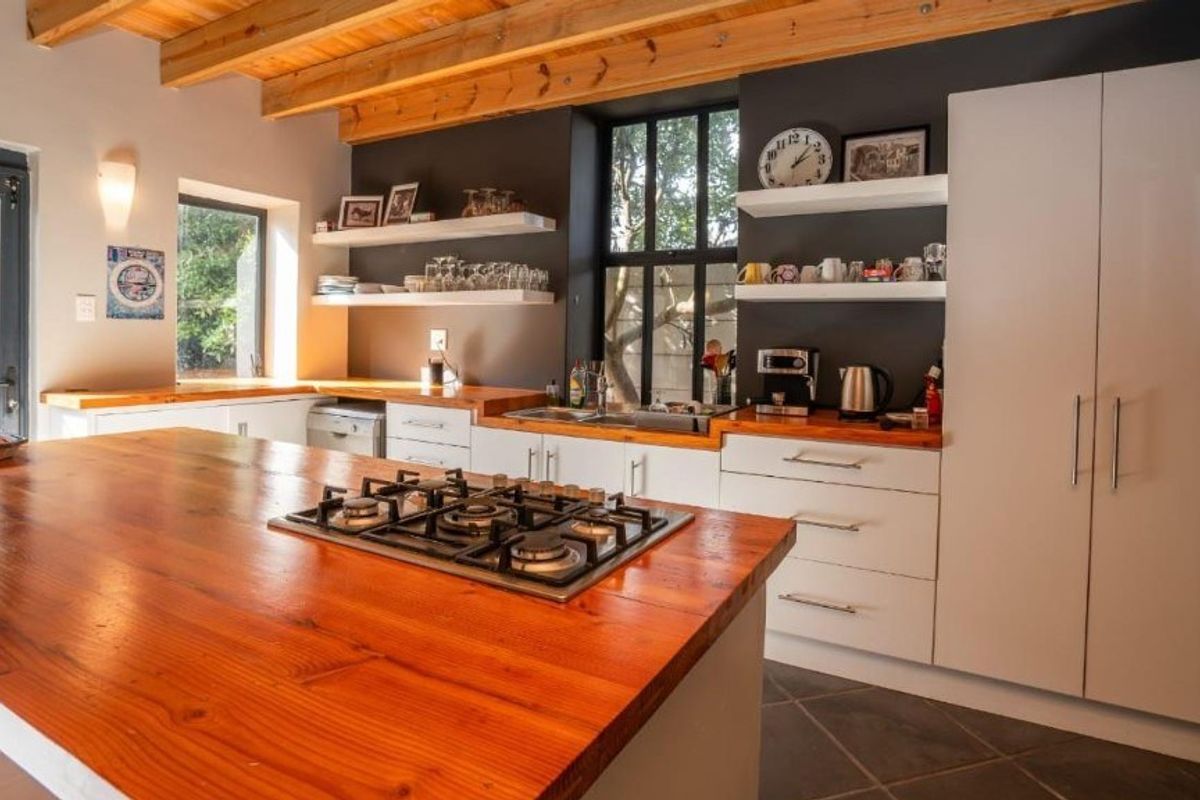 Modern kitchen featuring timber countertops, exposed ceiling beams, built-in gas hob, and ample cabinetry with floating shelving in a warm, contemporary design.