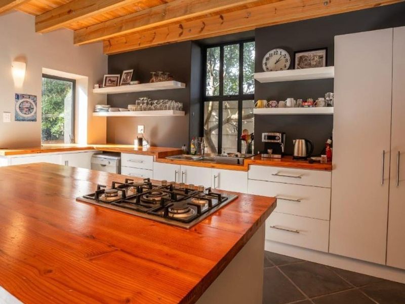 Modern kitchen featuring timber countertops, exposed ceiling beams, built-in gas hob, and ample cabinetry with floating shelving in a warm, contemporary design.