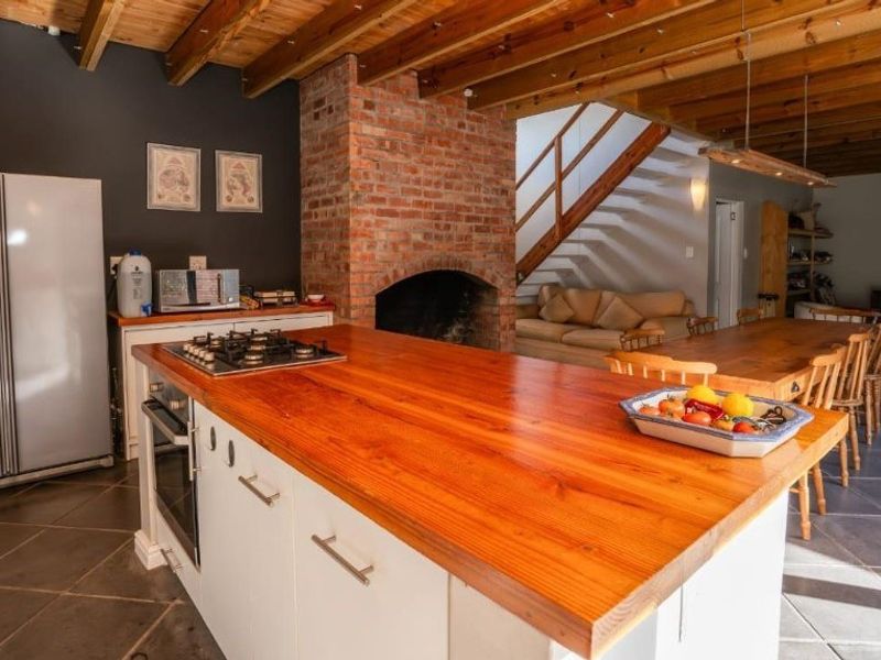 Spacious open-plan living area featuring a central kitchen island with gas hob, exposed timber ceiling beams, and a prominent brick fireplace.