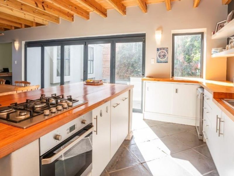 Spacious open-plan kitchen featuring timber countertops, gas hob, built-in oven, and large bi-fold doors opening to the exterior, complemented by exposed timber beam ceilings.
