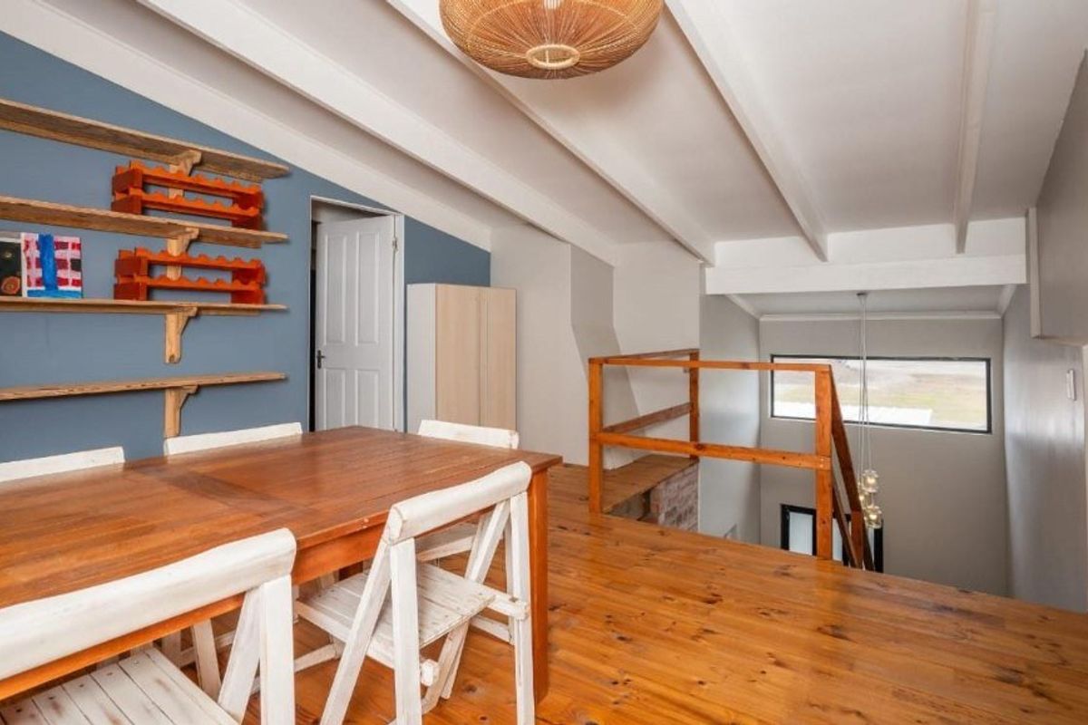 An open-plan mezzanine living area featuring exposed timber ceiling beams, polished timber flooring, and a wooden staircase railing overlooking the lower level.