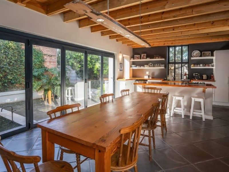Spacious open-plan kitchen and dining area featuring exposed timber beams, stone flooring, and large bi-fold doors opening to the rear garden.