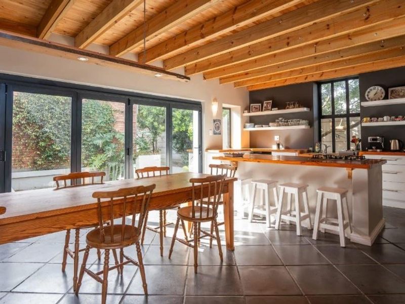 Spacious open-plan kitchen and dining area featuring exposed timber beams, modern cabinetry, a central island with a timber countertop, and large bi-fold doors to the garden.