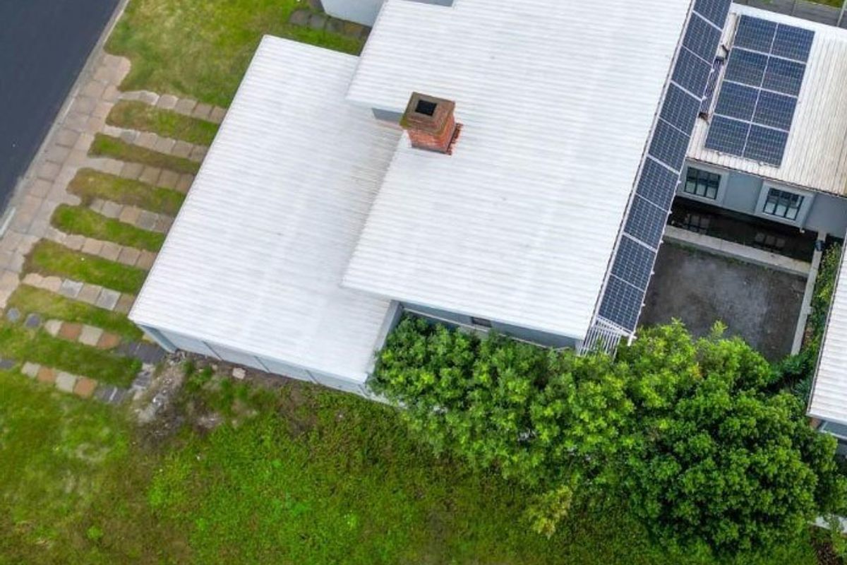 Aerial view of the property showcasing the roof structure, integrated solar panel system, brick chimney, and surrounding garden and driveway area.