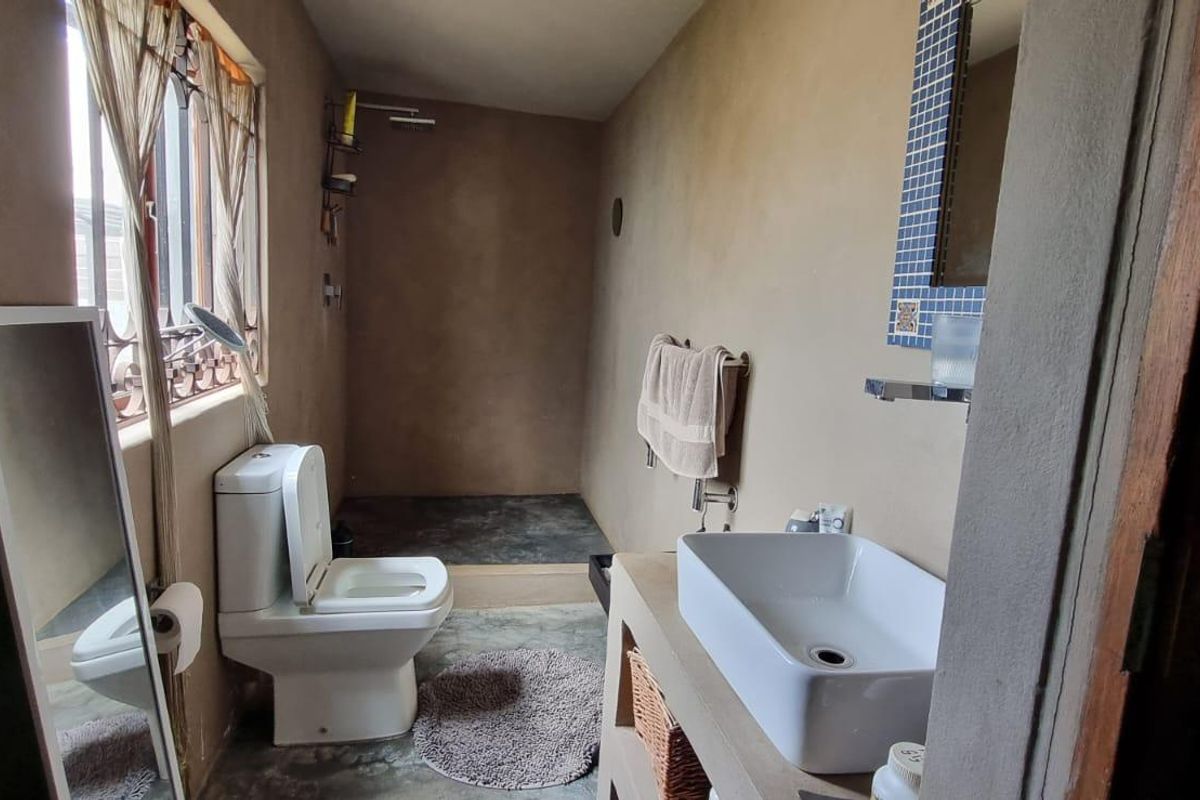 A rustic-style bathroom featuring a concrete vanity, vessel sink, and walk-in shower area with unfinished plaster walls.