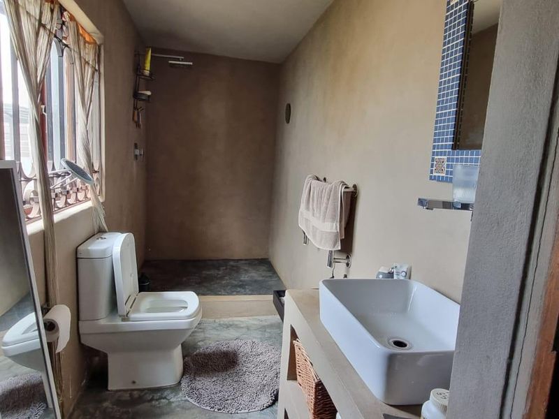 A rustic-style bathroom featuring a concrete vanity, vessel sink, and walk-in shower area with unfinished plaster walls.