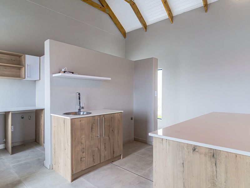 A modern, minimalist kitchen area featuring light wood cabinetry, stone countertops, an undermount sink, and striking exposed timber roof trusses under a vaulted ceiling.