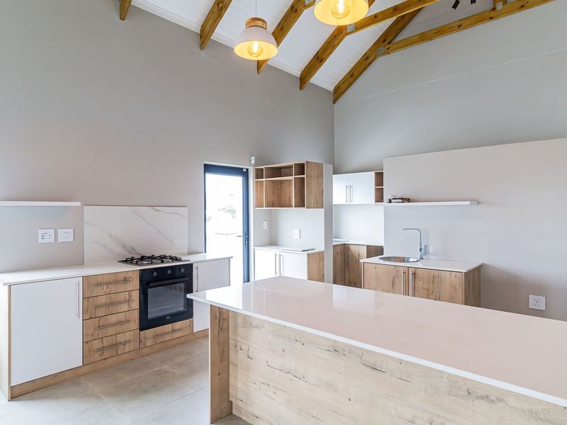 Modern kitchen featuring a large island, stone countertops, built-in oven, gas hob, and striking vaulted ceilings with exposed timber rafters.