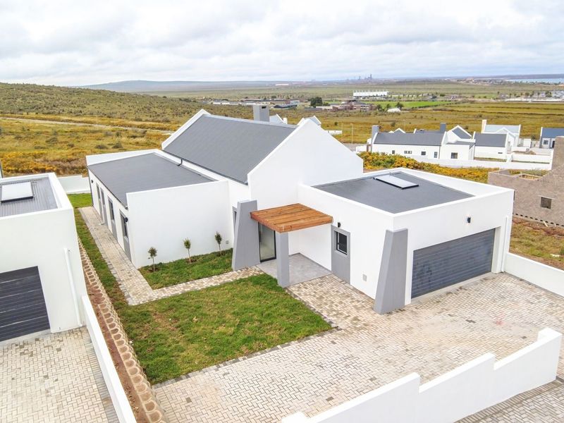 Aerial view of a modern residential property featuring a clean white facade, metal roofing, paved driveway, and a timber entrance pergola.