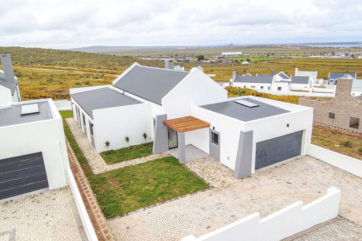 Aerial view of a modern residential property featuring a clean white facade, metal roofing, paved driveway, and a timber entrance pergola.