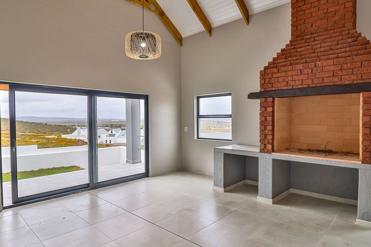 Spacious living area featuring a vaulted ceiling with exposed timber rafters, a large built-in brick fireplace, and sliding glass doors leading to a patio.