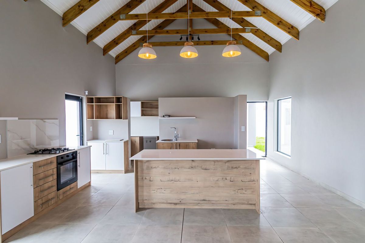 Modern open-plan kitchen featuring exposed timber trusses, a central island, built-in oven, gas hob, and sleek cabinetry under a high vaulted ceiling.