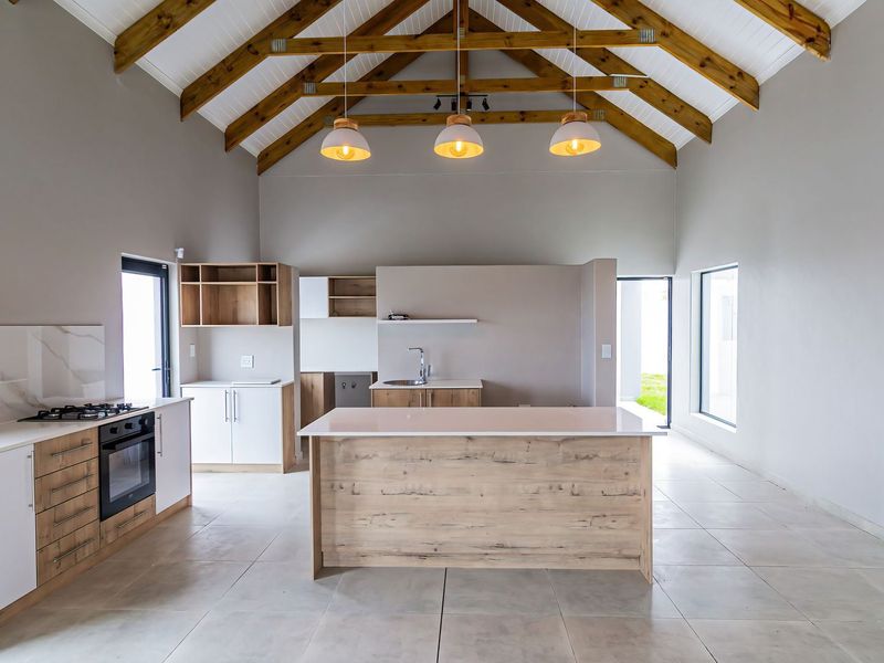 Modern open-plan kitchen featuring exposed timber trusses, a central island, built-in oven, gas hob, and sleek cabinetry under a high vaulted ceiling.