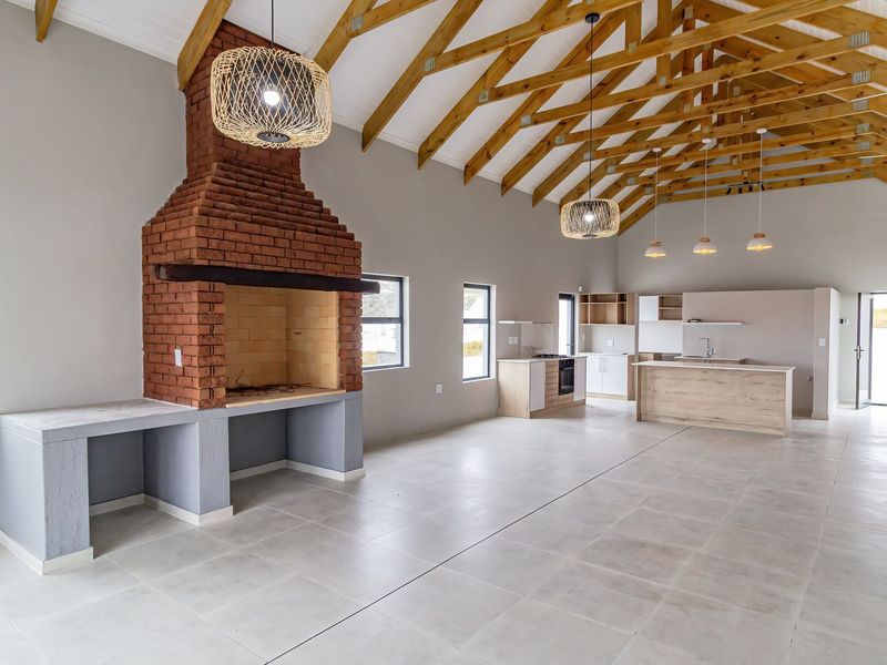 Spacious open-plan living area featuring exposed timber trusses, a large brick fireplace, and a modern kitchen with a central island and tiled flooring.