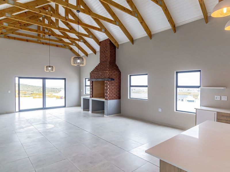 Spacious open-plan living area featuring high vaulted ceilings with exposed timber trusses, a brick fireplace, and modern kitchen finishes with stone countertops.