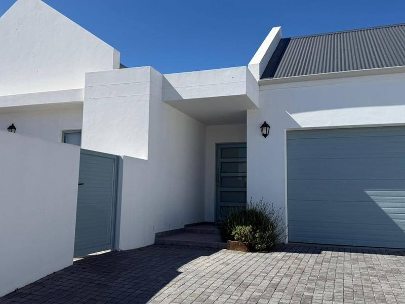 Modern front facade featuring a paved driveway, single garage, and a secure pedestrian entrance with clean white rendered walls and grey accents.