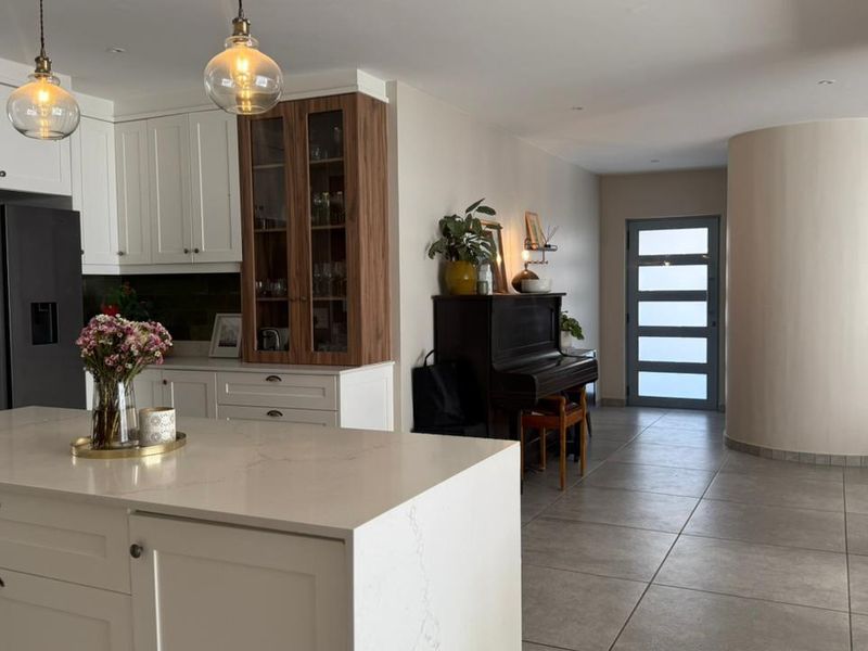 Modern open-plan kitchen featuring a central island with quartz countertops, shaker-style cabinetry, and tiled flooring, seamlessly connecting to the entrance area.