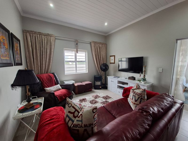 A comfortable living room featuring a tongue and groove ceiling, recessed downlights, and a window with security bars.
