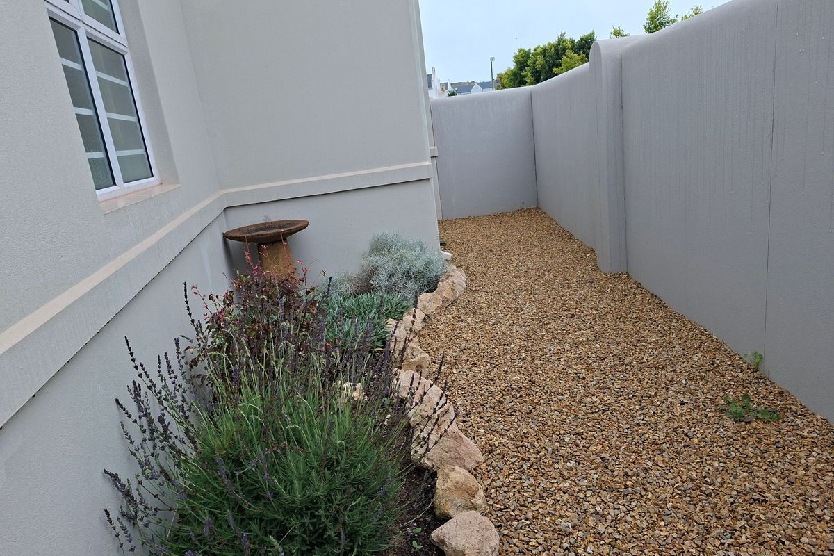 A side garden area featuring a gravel pathway, stone edging, and a clean boundary wall alongside the exterior of the house.