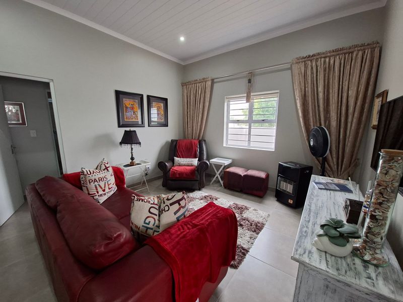 A cozy living room featuring tiled flooring, a tongue and groove ceiling, and a window fitted with security bars.