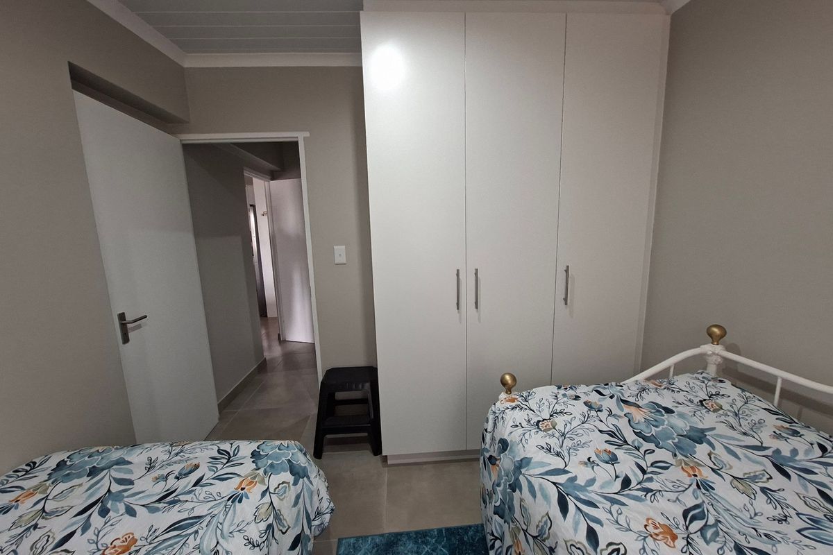 A bedroom featuring built-in white wardrobes, tiled flooring, and a tongue and groove ceiling, with access to an adjoining hallway.