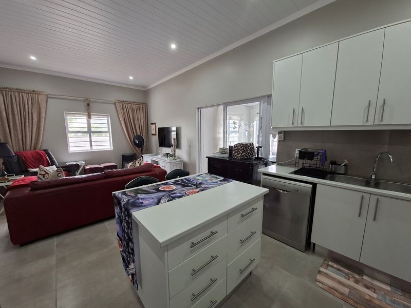 Open-plan living area featuring a modern kitchen with a central island, ample cabinetry, and tiled flooring, seamlessly connecting to the lounge space.