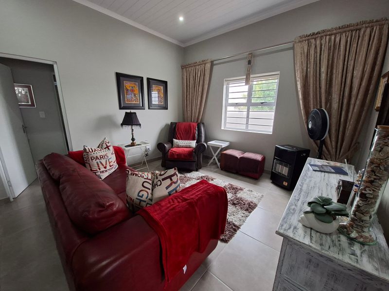 A comfortable living room featuring neutral tiled flooring, a tongue and groove ceiling, and a window fitted with security burglar bars.