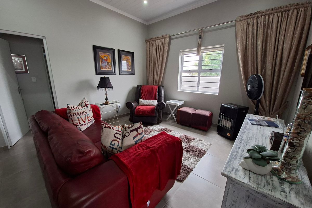 A comfortable living room featuring neutral tiled flooring, a tongue and groove ceiling, and a window fitted with security burglar bars.