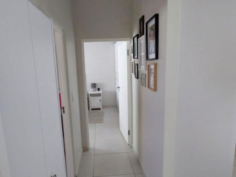 A clean, neutral hallway featuring tiled flooring and built-in storage cupboards, providing access to adjacent rooms within the home.