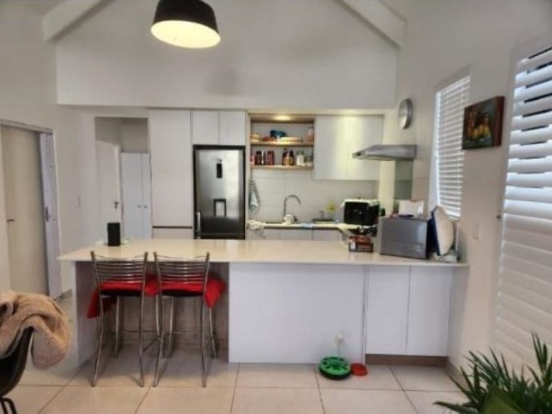 Modern kitchen featuring a central island, white cabinetry, stainless steel appliances, and vaulted ceilings with tiled flooring throughout.