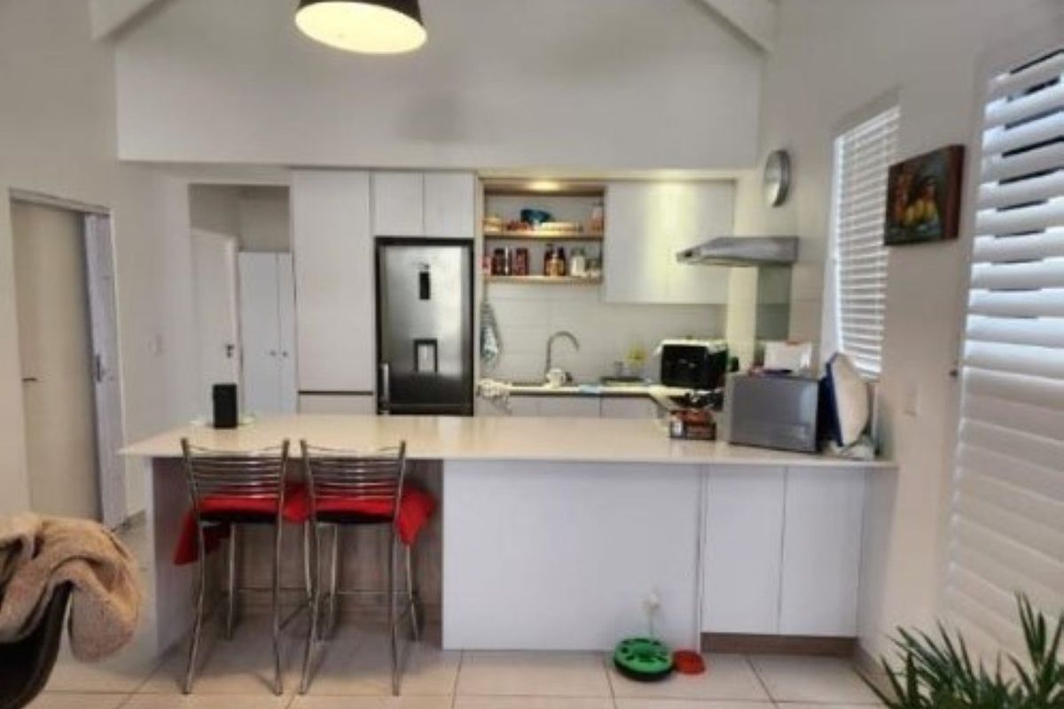 Modern kitchen featuring a central island, white cabinetry, stainless steel appliances, and vaulted ceilings with tiled flooring throughout.