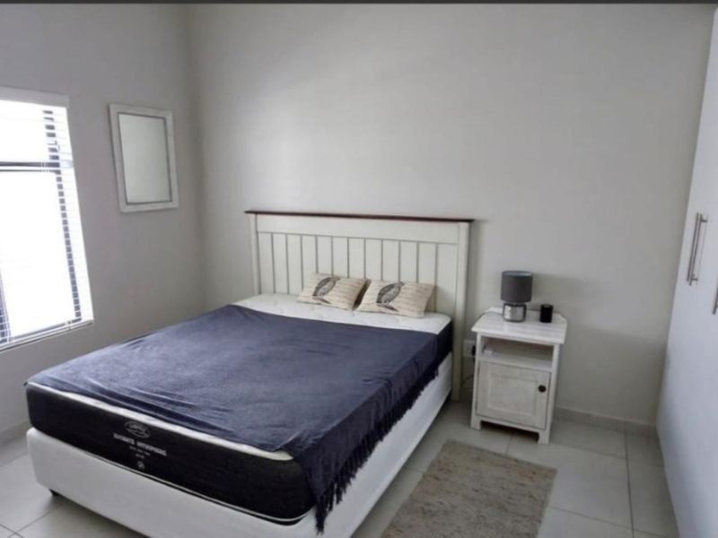 A clean and functional bedroom featuring neutral wall tones, tiled flooring, and a built-in wardrobe for storage.