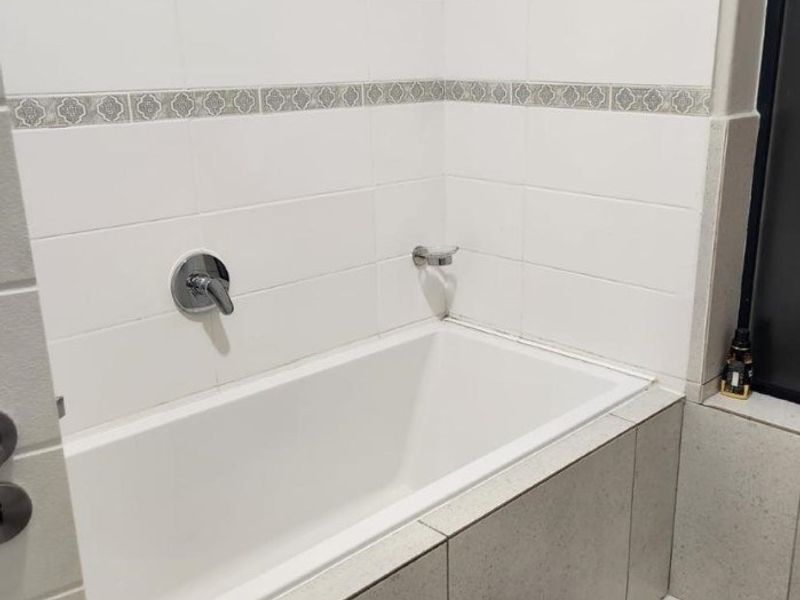 A clean, modern bathroom featuring a built-in bathtub with wall-mounted fixtures, complemented by white wall tiles and a decorative accent border.