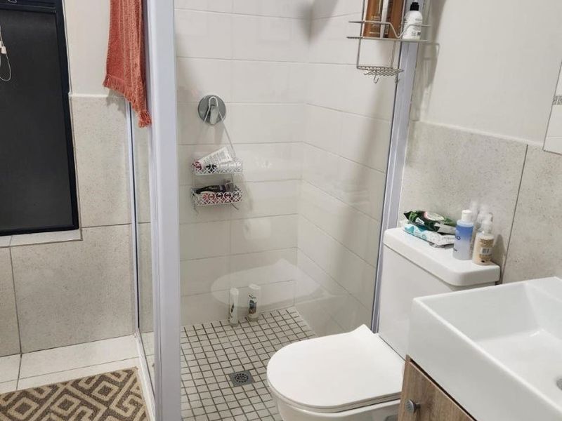 A functional bathroom featuring a glass-enclosed shower, modern vanity with basin, and neutral wall and floor tiling.