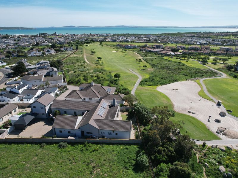 Aerial view of a residential property situated adjacent to a golf course with coastal views in the background.