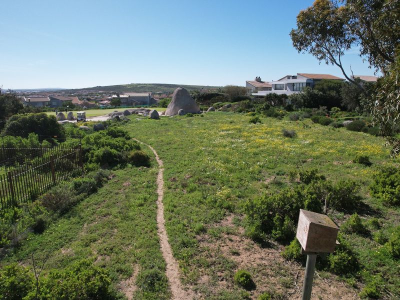An aerial view of a vacant residential plot featuring natural vegetation, rock formations, and perimeter fencing in a coastal estate setting.