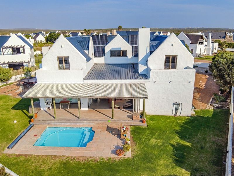 Aerial view of a white double-story house featuring a swimming pool, covered patio, timber decking, and roof-mounted solar panels in a coastal estate setting.