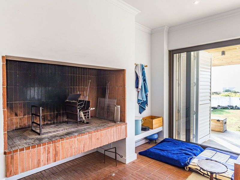 Covered patio area featuring a large built-in brick braai, tiled flooring, and sliding glass doors providing seamless access to the outdoor garden space.