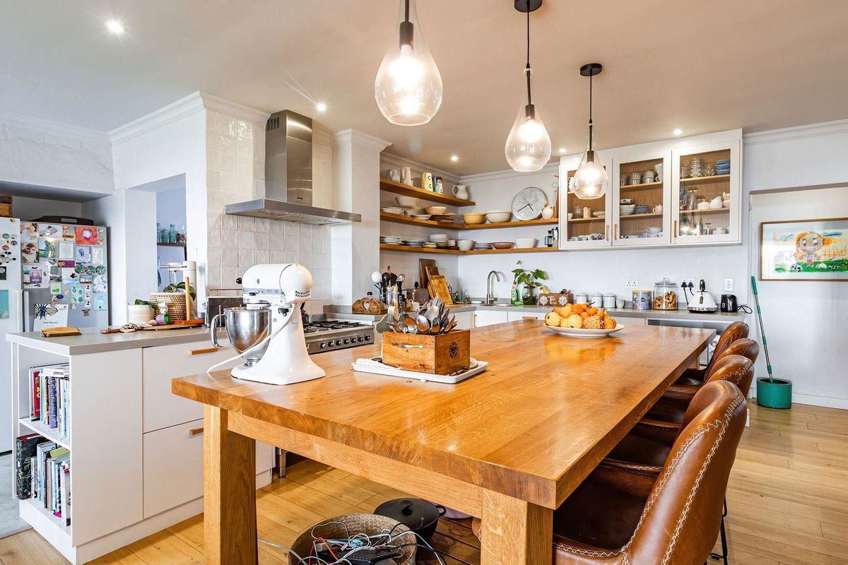 A bright, modern kitchen featuring a large central island, open shelving, glass-fronted cabinetry, and high-quality hardwood flooring with integrated stainless steel appliances.