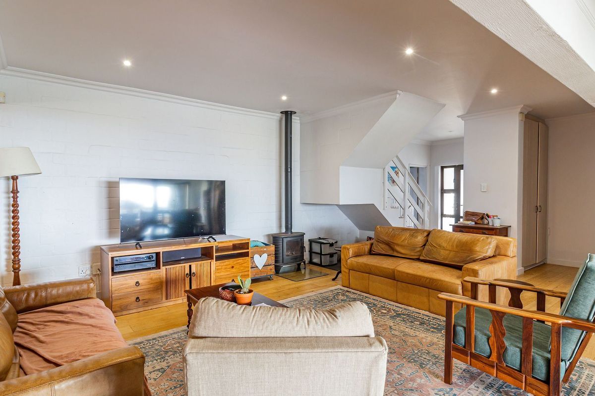 Spacious living room featuring timber flooring, a built-in wood-burning fireplace, and a staircase, creating a warm and inviting atmosphere.