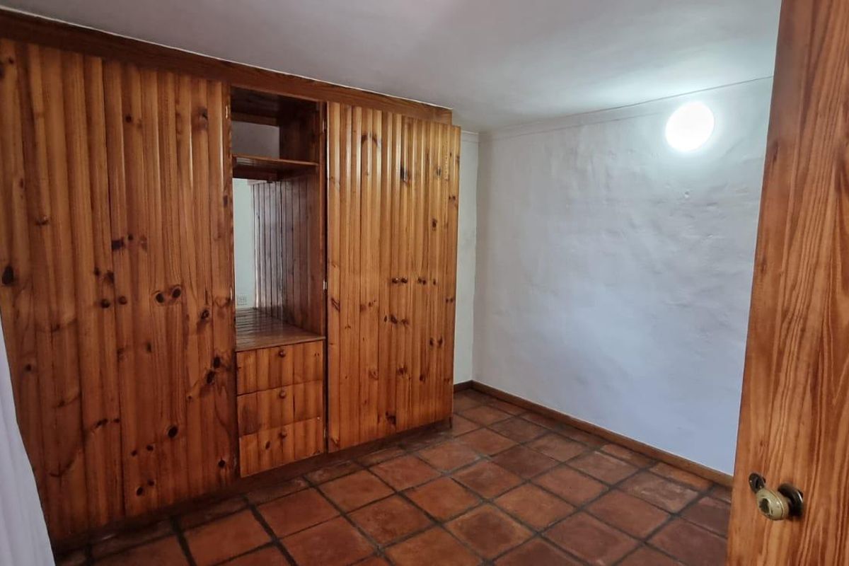 A vacant bedroom featuring built-in wooden cabinetry, terracotta tile flooring, and a simple white wall finish.